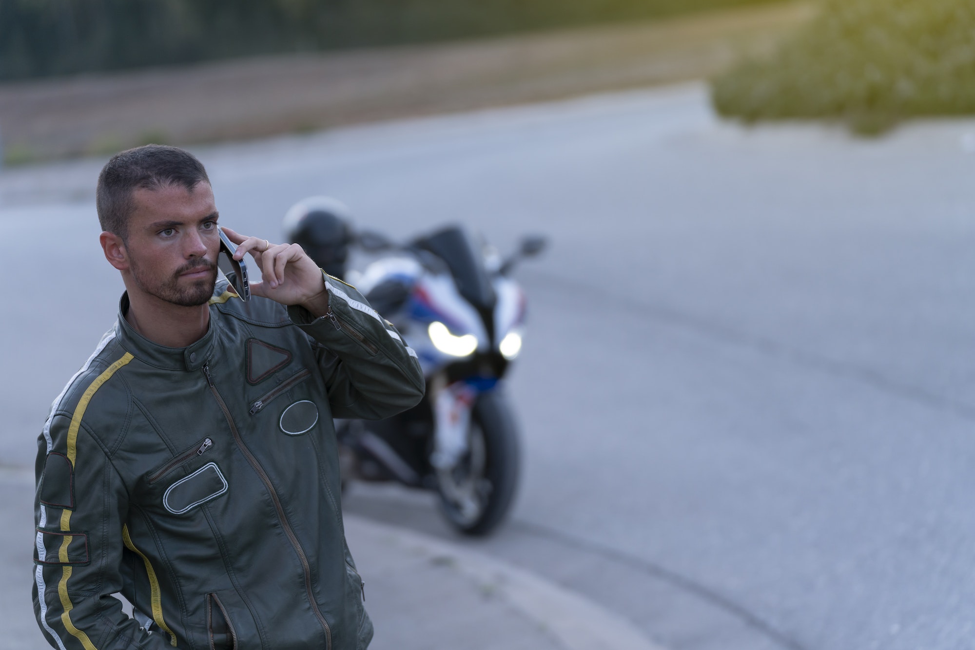 Jeune homme en panne de moto sur la route en train de parler au téléphone